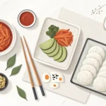 Stylized Korean food items and design tools arranged neatly on a light background, representing the...