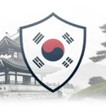 Stylized shield icon with Korean colors next to a helping hand symbol, representing industrial accid...
