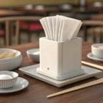 A Korean restaurant table setting comparing a thin paper napkin from a dispenser to a thicker cloth...