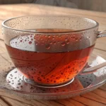 A steaming glass cup of red Rooibos tea sits on a wooden table in a modern Korean cafe setting, illu...
